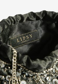 Fekete selyem táska belseje ráncolt éllel, ezüst flitterekkel, fém lánc részletekkel és egy jól látható LIPSY címkével.