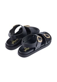 Sandalias negras con dos correas ajustables y hebillas doradas. La plantilla texturizada y la suela gruesa ofrecen comodidad y soporte.