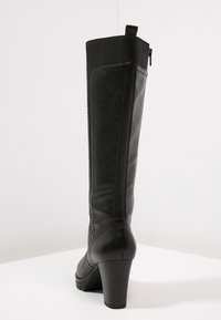 Botas de tacón alto de cuero negro con cierre de cremallera y panel elástico, que presentan una textura suave y un diseño estilizado.