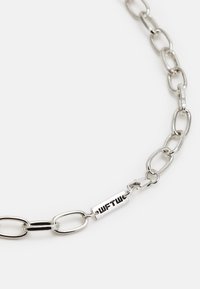 Colar de corrente prateada com elos ovais, acabamento polido, com um fecho marcado "WFTW" numa etiqueta retangular.