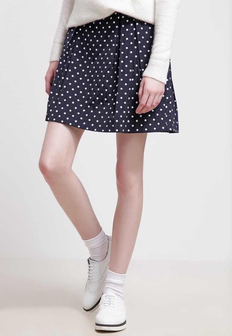 Gonna a pois navy con pieghe, realizzata in tessuto leggero. Accenti bianchi visibili su scarpe e calze.
