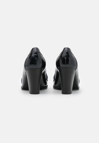 Černé lakované vysoké podpatky s zakřivenou siluetou a texturovaným podpatkem. Na boku mají dekorativní prvek.