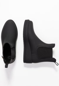 Botas de tobillo de goma negras con un acabado suave, lados elásticos y bucle para tirar. Presentan una suela texturizada para agarre y comodidad.