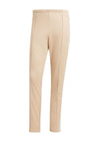 Pantalones deportivos beige con una textura suave, cinturilla elástica y franjas laterales. Pequeño logo blanco en el muslo izquierdo, diseño ajustado.