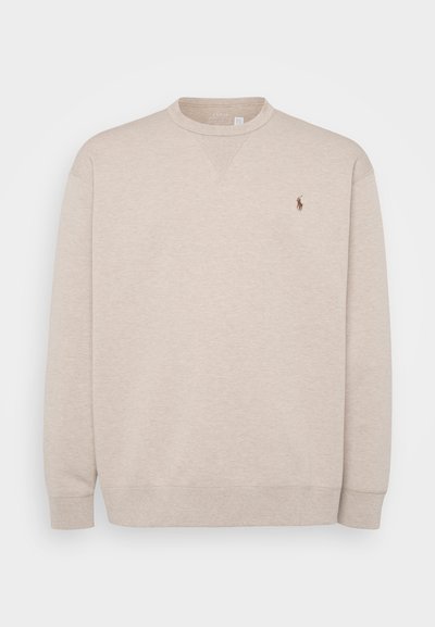 Beige genser laget av myk stoff, med rund hals, lange ermer og en liten brodert logo på brystet.