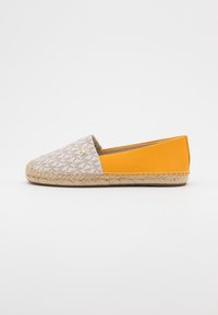 Espadrillas piatte beige e giallo senape con motivo monogram sul dito e suola in juta intrecciata su sfondo bianco.