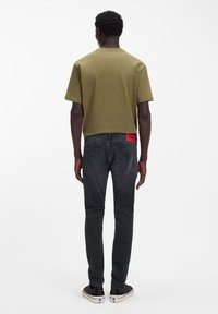 Oliivinvihreä, lyhythihainen t-paita, yhdistetty tiukasti istuviin mustiin farkkuihin, joissa on punainen logopainatus vyötäröllä ja kontrastiväriset saumat.