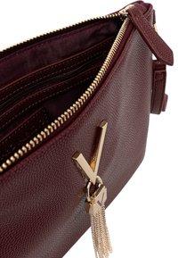 Borsa in pelle testurizzata bordeaux con hardware dorato, zip e dettaglio a nappina. L'interno presenta più tasche per un'organizzazione ottimale.