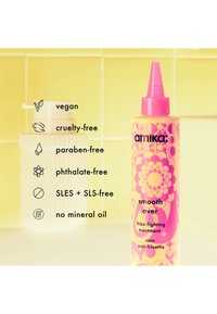 Amika Smooth Over anti-frizz behandelingsfles met roze dop, kleurrijk bloemmotief en tekst die veganistische, dierproefvrije en chemische-vrije eigenschappen opsomt.