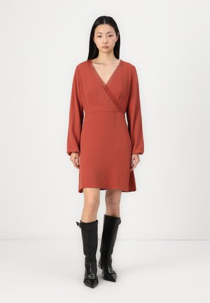 Rust-colored dress with long sleeves, v-neckline, and lace detailing. Paired with knee-high black leather boots featuring pointed toes.