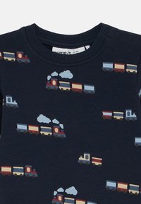 Σκούρο γαλάζιο ύφασμα με επαναλαμβανόμενο μοτίβο κόκκινων, μπλε και μπεζ παιχνιδιών τρένων που εκπέμπουν λευκό καπνό.