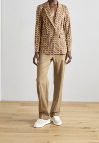 Bruine geruite blazer met een getaillede pasvorm, met een notch-kraag en twee zakken, gecombineerd met beige broek en witte sneakers.