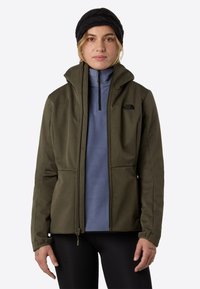 Olive green soft-shell jacket with a high collar, black zip hardware, and zippered hand pockets, layered over a light blue fleece top.