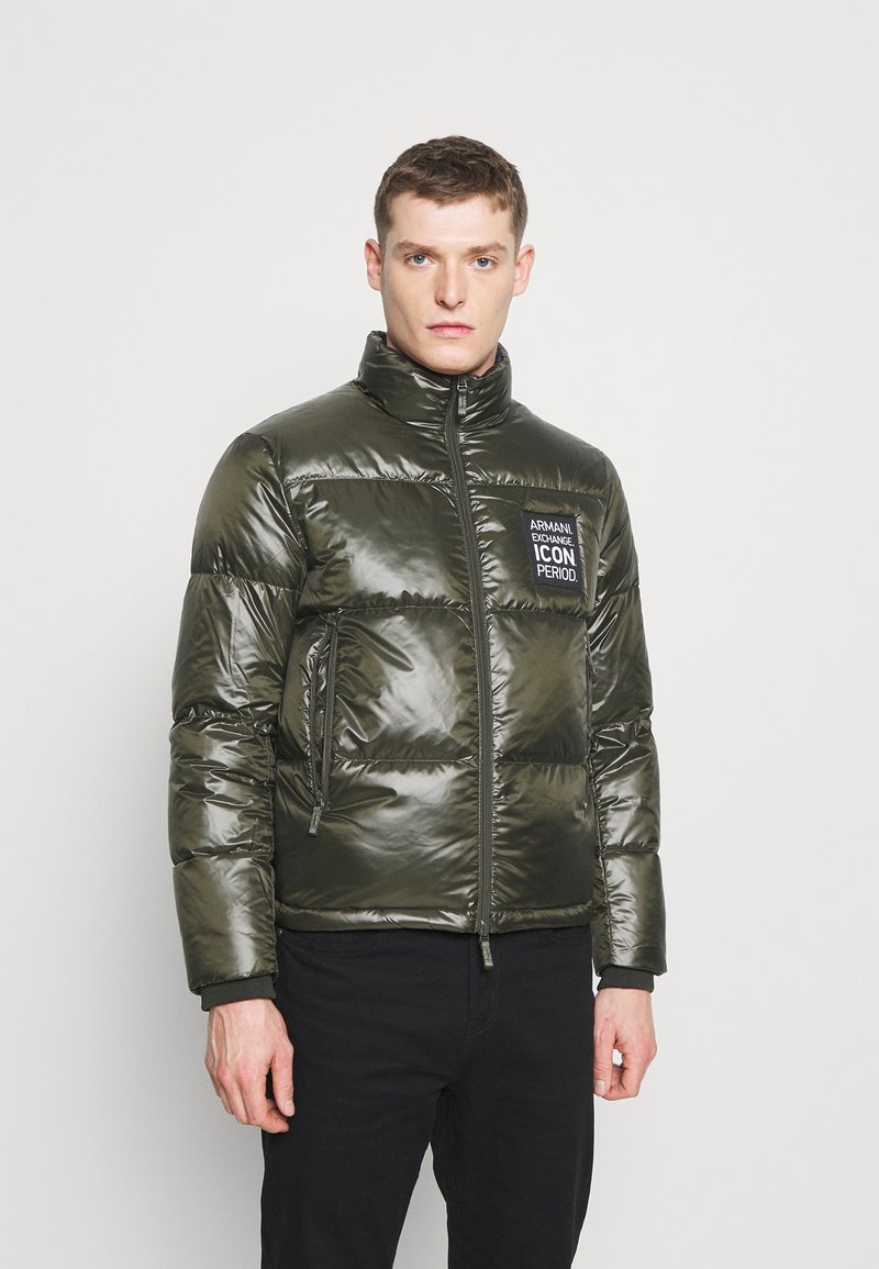 Giacca a vento verde con colletto alto, texture lucida, zip frontale e una patch con "Armani Exchange ICON PERIOD" sul petto.