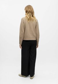 Beige knit sweater with a loose fit and dropped shoulders, paired with wide black trousers, viewed from the back against a white background.