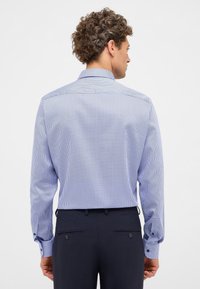 Lichtblauw shirt met een klein, geometrisch patroon, lange mouwen en knoopmanchetten. De stof heeft een zachte textuur. Draag het met donkere broek.