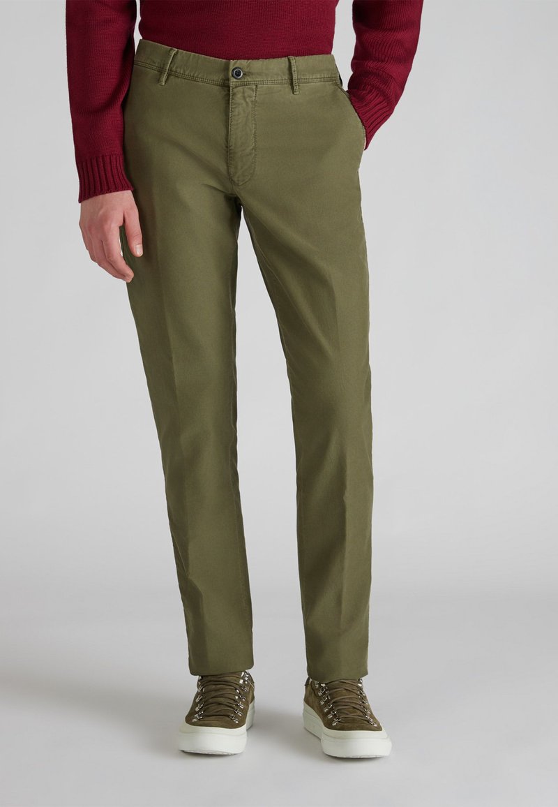 Oliwkowe chinosy o prostym kroju, z zapięciem na guzik, kieszeniami bocznymi i gładką bawełnianą tkaniną. W połączeniu z teksturowanymi sneakersami.