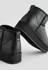 Schwarze Knöchelboots aus strukturiertem Leder mit einem Futter aus Kunstfell, flachen Gummisohlen und gesteppten Details an der Oberseite.