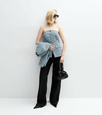Top azul y blanco sin tirantes de tweed con una manga grande y fluida, combinado con jeans anchos negros y un pequeño bolso negro.