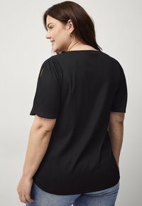 Zwarte short-sleeve top van een textuurstof, met uitsparingen op de schouders en een afgeronde zoom, gecombineerd met een blauwe jeans.
