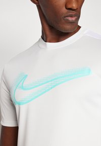 Maglietta sportiva bianca realizzata in tessuto liscio, con un grande logo Nike turchese caratterizzato da un motivo a gradiente a pois sul davanti.