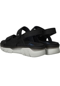 Sandales noires avec des brides ajustables, fabriquées en matériau doux, dotées d'une semelle grise rembourrée avec une surface texturée et un design angulaire.