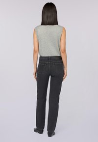 Top sin mangas gris combinado con unos jeans de mezclilla gris oscuro. Los jeans tienen un corte clásico y bolsillos traseros con un parche de cuero en la cinturilla.
