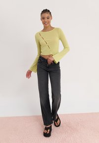 Lysegrønn langermet crop topp med utskjæringsdetaljer, kombinert med høy midje mørkegrå jeans og svarte platåsandaler.
