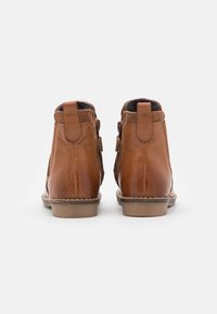 Botines de cuero marrón con acentos de ante, punta redondeada y un tacón bajo. Presentan costuras y una lengüeta trasera para facilitar el calzado.