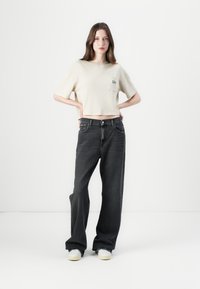 Lichtbeige cropped t-shirt met een zak en zwarte high-waisted wijde jeans. De jeans hebben een klassiek vijf-pocketontwerp.