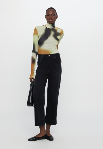 Black high-waisted jeans paired with a fitted, multicolored long-sleeve top featuring green, orange, and black abstract patterns.