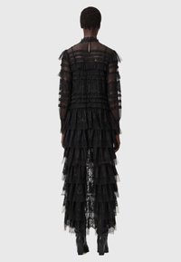 Svart spetsklänning med ett lager av volangdesign, långa genomskinliga ärmar och en nyckelhålsdetalj på ryggen. Bärs med svarta klackkängor.