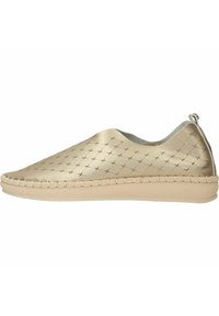 Instapper met een metalen gouden bovenkant met geperforeerde kruispatronen, een beige flexibele buitenzool en decoratieve stiksels langs de rand.