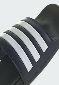 Black slide sandal featuring a textured strap with three prominent white stripes. The sole is smooth and the design is minimalistic.
