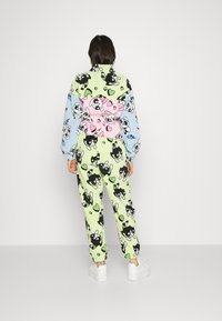 Buntes Loungewear-Set bestehend aus einem übergroßen Pullover und passender Hose. Der Stoff zeigt verspielte Cartoon-Muster in verschiedenen Farben wie Grün, Blau und Pink.