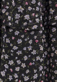 Tissu noir à motif floral avec de petites fleurs blanches et roses. Matière légère et texturée avec des détails froncés.