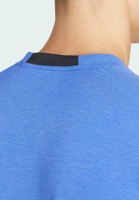 Koninklijk blauwe t-shirt met een ronde hals, voorzien van een zwarte accent bij de achterkant van de kraag. De stof lijkt zacht en licht gestructureerd.