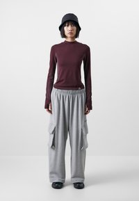 Mörkröd långärmad topp med texturerade sidopaneler, parat med lösa grå cargobyxor med stora sidofickor. Svart bucket hat och sneakers.