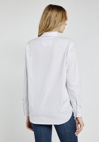 Biała koszula z guzikami, pokryta małymi czerwonymi i czarnymi kropkami, z długimi rękawami, zaokrąglonym dołem oraz kołnierzykiem na plecach poprawiającym dopasowanie.