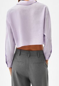 Cropped lavender shirt with a collar and long sleeves, paired with high-waisted gray trousers featuring a smooth fabric and subtle pockets.