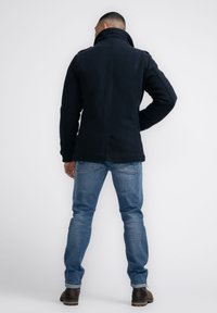 Chaqueta de forro polar azul marino oscuro con cuello alto y mangas largas, combinada con jeans azul claro y botas marrones. Diseño sencillo, sin patrones.