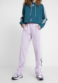 Teal kort hoodie med vit dragsko och tre ränder på ärmarna. Ljuslila träningsbyxor med sidostripes och fickor.