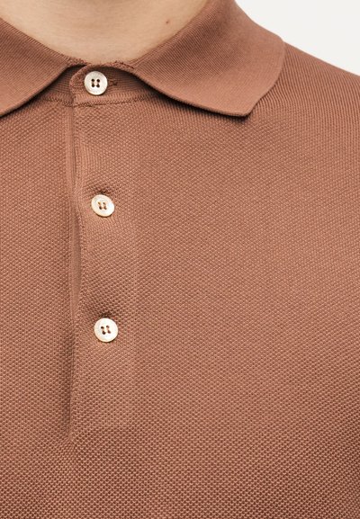 Gros plan sur un polo en maille marron avec trois boutons blancs et un col plié.