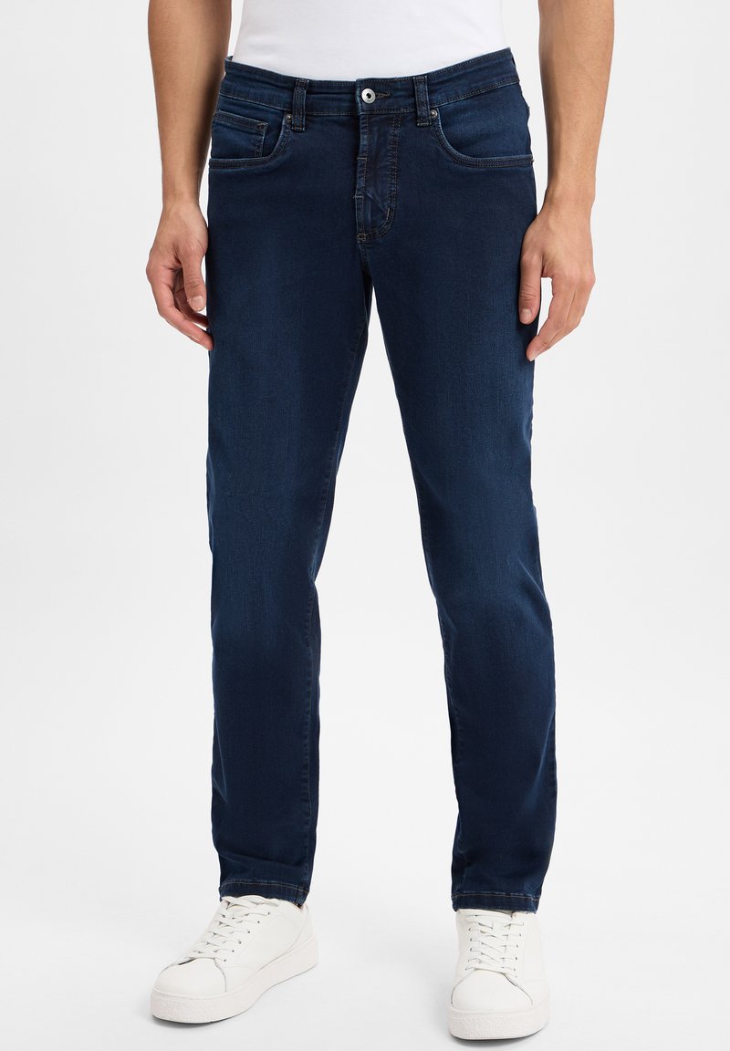 Dunkelblaue Jeans mit geradem Schnitt, fünf Taschen und sichtbaren Nähdetails, kombiniert mit weißen Sneakers.