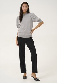 Pull en tricot gris clair à manches bouffantes, associé à un pantalon noir ajusté et des mules noires à talons. Texture lisse, design minimal.