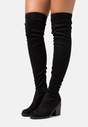 Botas negras de ante hasta la rodilla con un tacón grueso, silueta ajustada, detalles de cremallera sutil y textura suave.