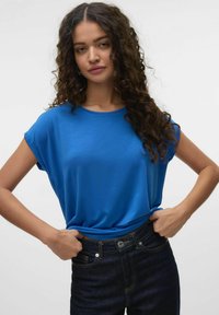 Blauwe top met korte mouwen en een ronde hals, gemaakt van zachte stof, gecombineerd met donkere spijkerbroek met een aansluitende taille.