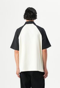 Short-sleeve polo shirt featuring a black collar and raglan sleeves, with a cream body. Smooth texture, casual fit.