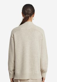 Beżowy sweter z wysokim kołnierzem i prążkowanymi mankietami. Miękka, teksturowana tkanina o luźnym kroju, z przeszyciem na plecach.