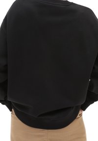 Sudadera negra con cuello redondo y puños acanalados. Textura suave y ajuste ligeramente holgado, con una cintura que se ajusta de manera ceñida.